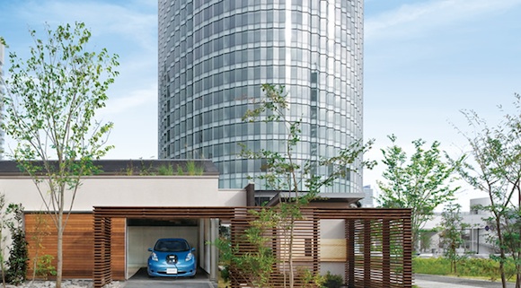 elektromobil Nissan Leaf nabíjí rodinný dům, v pozadí mrakodrap